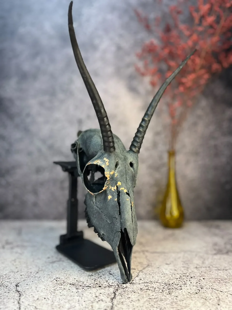 Antelope skull with long ridged horns, finished in weathered blue-grey with gold-leaf accents, on a display stand