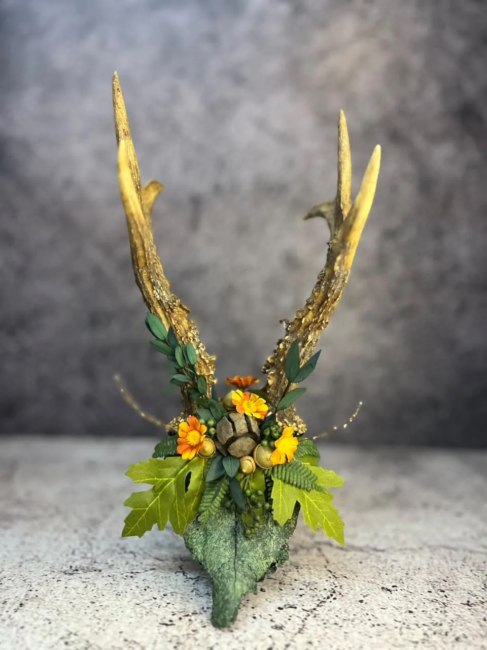 Antlered skull finished in moss-green texture and dressed with foliage and orange flowers