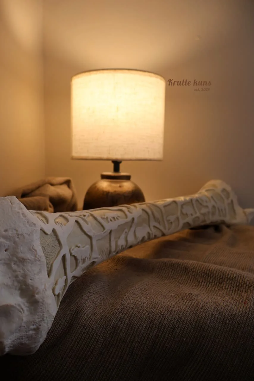 Giraffe bone carved in relief with a pattern of animals, lit by a lamp in the background