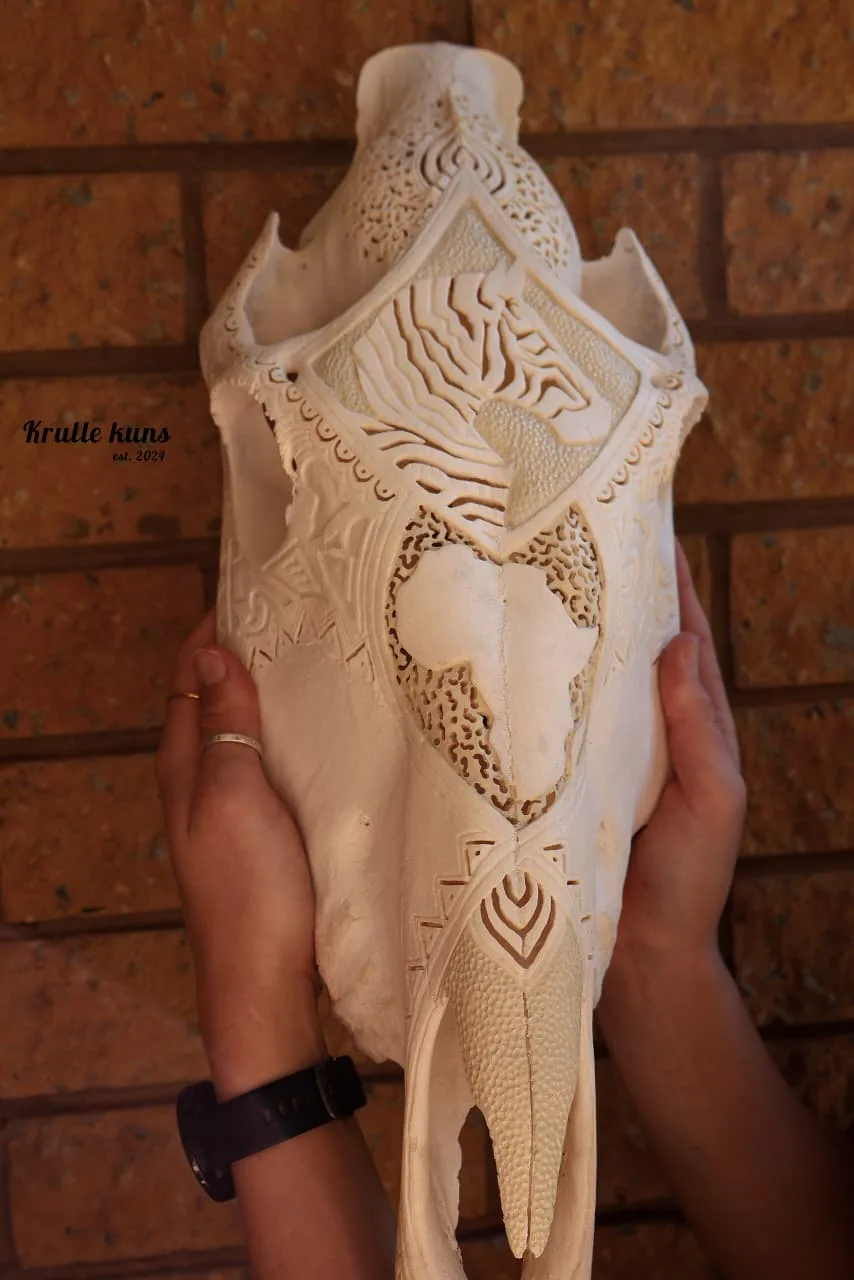 Zebra skull carved with zebra stripes and a map of Africa, held in two hands against a brick wall